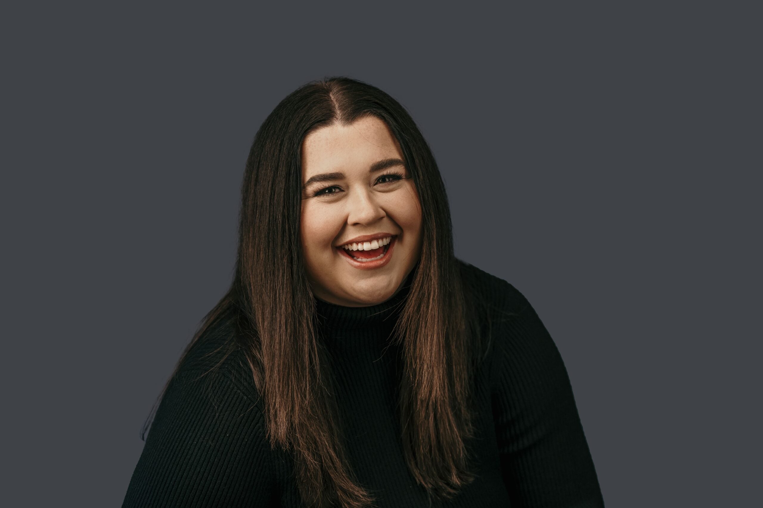 Founder McKenzie smiling (Causasian woman headshot, brown hair, long sleeve black turtleneck)