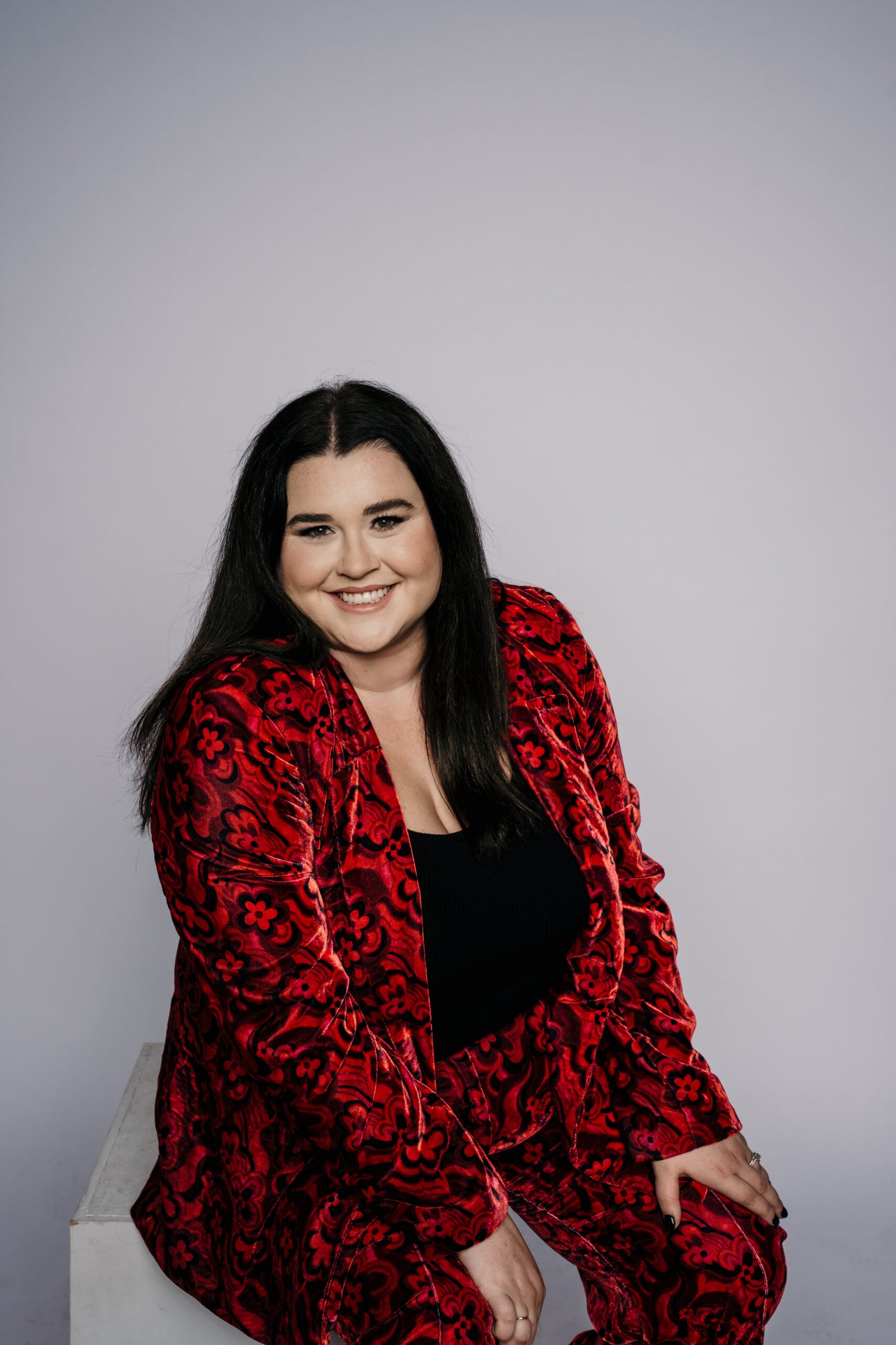 Covalent Creative Founder, McKenzie Jevnikar. Caucasian woman with dark hair wearing a red detailed velvet suit with a black top.